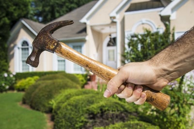 Mans hand holding hammer in front of a house indicating home improvement and maintenance.-1