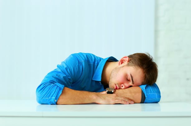 Young tired businessman sleeping at workplace in office